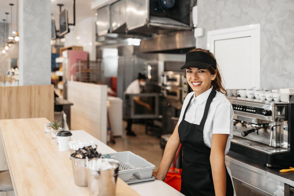 Beautiful and happy young female worker working in a bakery or fast food restaurant and using coffee machine.